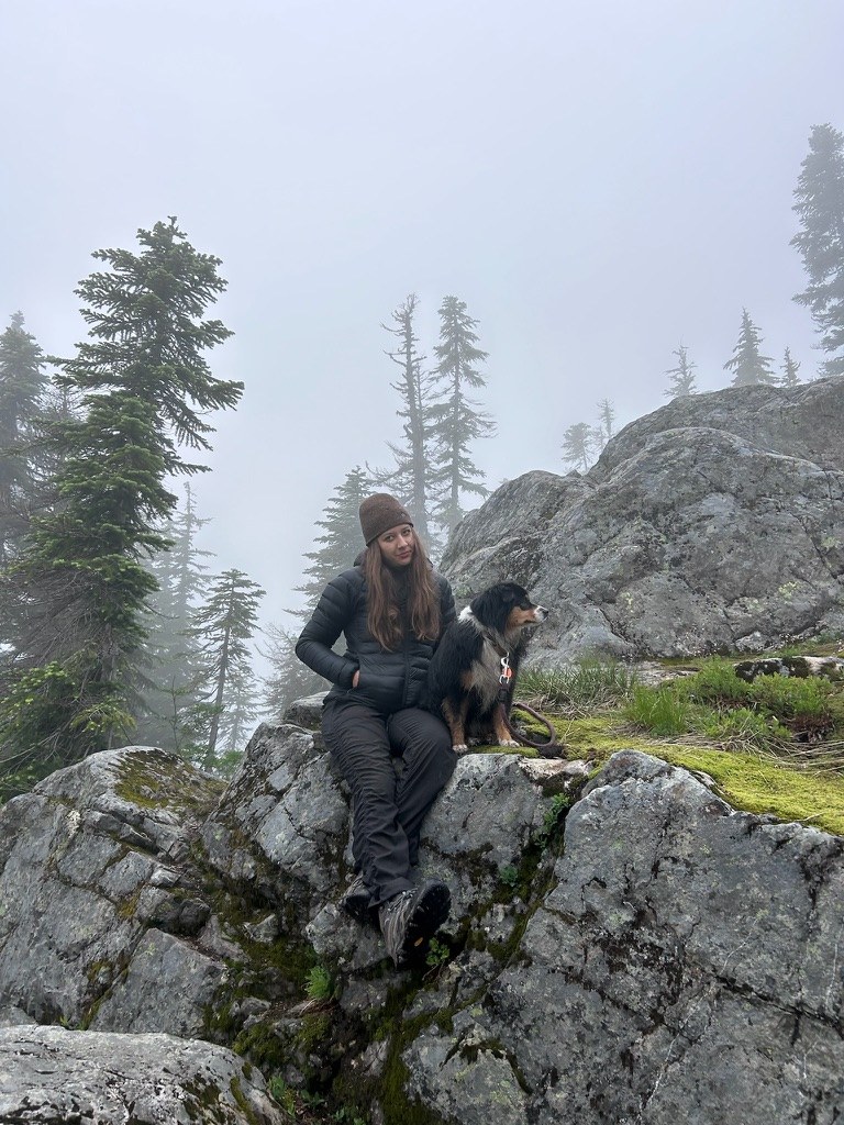 Lia Simone Bacon sitting on a granite outcrop with her dog on a misty mountain trail